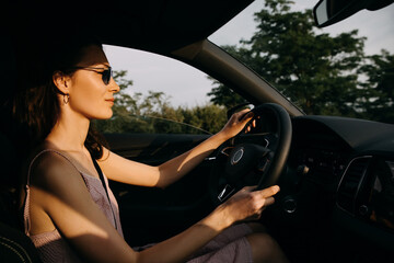 Wall Mural - Young woman driving on a highway at the sunset. Driving school concept.