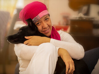 latin woman hugging her pet, woman with pink scarf on her head due to breast cancer