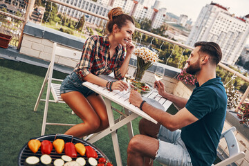 Sticker - Cute young couple in casual clothing enjoying romantic dinner and smiling while enjoying romantic dinner on the rooftop patio outdoors