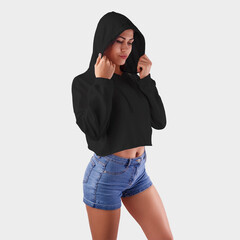 Wall Mural - Mockup of a female crop top on a girl wearing a hood, fashionable black clothes on a white background in the studio.
