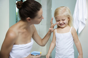 Wall Mural - Mom applying cream on her daughter face in bathroom. 