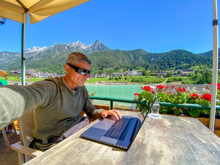 Canvas Print - Relaxed man working with laptop in front of a mountain lake. Business and tourism concept