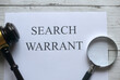 Top view of gavel,magnifying glass and paper written with Search Warrant on white wooden background.