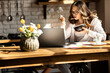 © shunevich - Beautiful young woman have breakfast while working on laptop at the kitchen