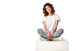 cheerful woman in jeans sitting on cube and smiling isolated on white
