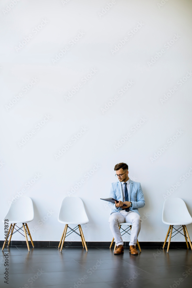 Young man sitting in the waiting room with a folder in hand before an interview - obrazy, fototapety, plakaty 
