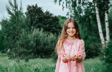 girl with long hair in a pink dress smiles against a background of greenery