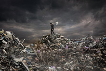 Global Warming Concept. A Man With A White Flag Stands On A Mountain Of Garbage On A Gloomy Background.