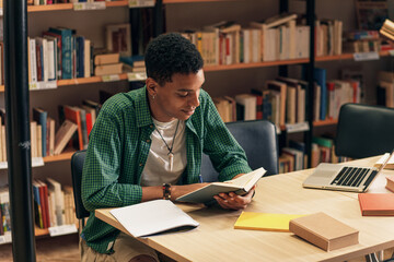 Wall Mural - Young male student study in the library reading book.