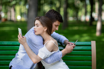 Wall Mural - Gadget addicted couple using mobile phones while embracing on bench at park