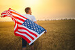 Man holding American flag blowing and waving in farm agricultural wheat field. Selectove focus on flag