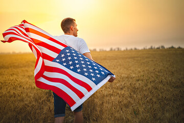 Wall Mural - Man holding American flag blowing and waving in farm agricultural wheat field. Selectove focus on flag