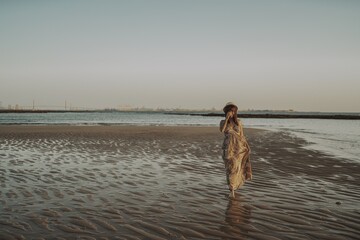 Wall Mural - Young female with tattoos wearing a dress and straw hat on blurred ocean background