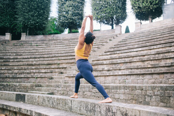 Wall Mural - Rear view of spanish woman in track suit standing in yoga pose breathing and enjoying recreation outdoors, 20s female practise yoga feeling inspiration and balance in asana keeping body shape