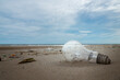 Used light bulb and garbage on the beach with soft wave and blue sky with cloud.