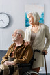 © LIGHTFIELD STUDIOS - senior woman with walking stick touching shoulder of disabled husband sitting in wheelchair