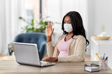 Wall Mural - quarantine, remote job and pandemic concept - african american woman wearing face protective medical mask for protection from virus disease with laptop computer having video call at home office