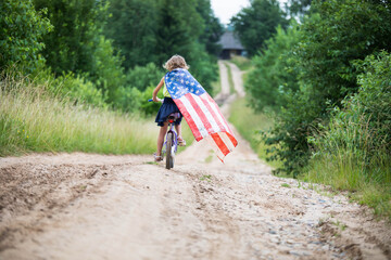 Symbol of celebration 4 fourth of july. Young Girl riding bicycle with american flag in hand