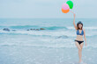 © KASEMKRIT - Asian woman wearing a blue bikini Holding a balloon standing at the beach in summer and smile happily