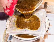 Close Up View Of Beekeeper Pouring Melted Beeswax (cera Alba) Through Gauze Filter To Clean Old Used Wax And Reuse It To Make New Honeycomb Foundations.