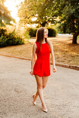 Photosession of a pretty girl walking in the city at sunset in a red dress with beautiful hair