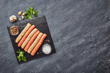 Wall Mural - Raw butchers sausages on slate with herbs. Overhead view