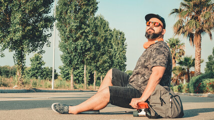 Curvy man in shorts sitting on a skateboard smiling.