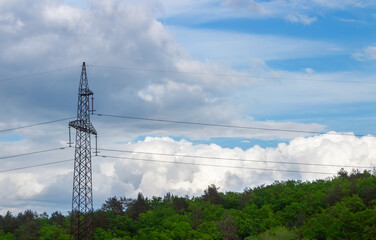 High voltage pole with wires against a cloudy sky and forest