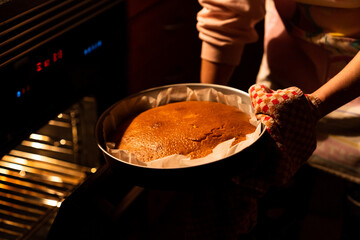 Woman taking a delicious freshly baked homemade cake out of the oven. Preparing a homemade cake at home in the kitchen with warm light.