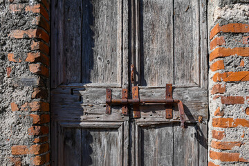 Poster - Close-up of an old wooden door ruined by time with a rusty lock and a brick wall, Italy