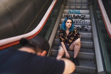 Poster - Caucasian female with blue hair posing on an escalator and a photographer taking her picture