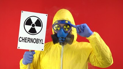 Wall Mural - Man in Protective Chemical Suit, Mask and Banner in Hands. Chernobyl Turns a Finger At the Temple. Smoke Around Man.