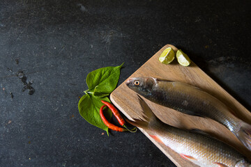 Different view of raw fish on black background on a wooden platter.