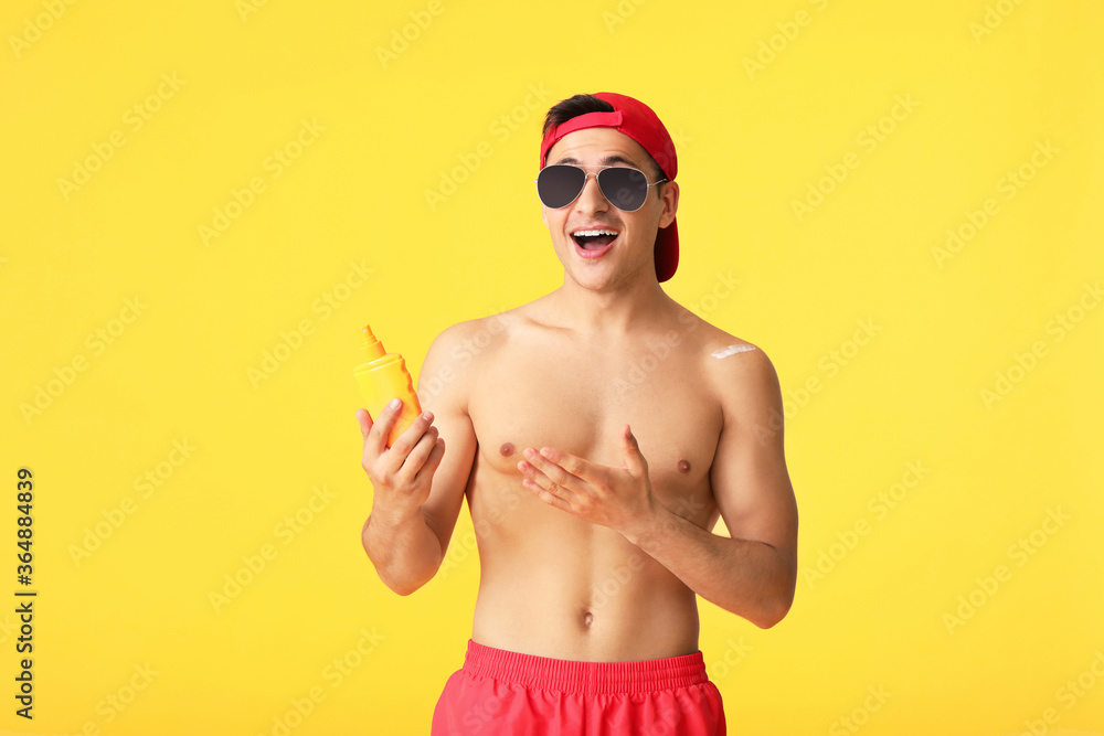 Happy young man with sun protection cream on color background