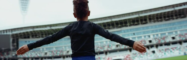 Wall Mural - Portrait of cute little black kid boy spreading hands on a large football stadium, dreaming of becoming professional player, soccer star. Shot on RED camera with anamorphic lens