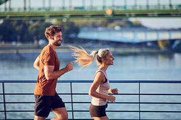 Modern woman and man jogging / exercising in urban surroundings near the river.