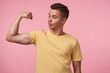© timtimphoto - Studio photo of young handsome brown haired man looking proudly at his hand while demonstrating his strong biceps, standing over pink background in casual wear