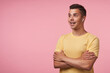 © timtimphoto - Studio shot of young brunette male with headphones looking emotionally ahead with wide smile and keeping hands folded on chest, isolated over pink background
