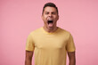 © timtimphoto - Portrait of young excited short haired man with short haircut frowning his face while screaming madly, standing against pink background with hands down