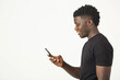 © Alexandr - handsome young african male in a black t-shirt on a white background with a smile with a phone in his hand
