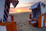 Fototapeta Do pokoju - Wschód słońca na wybrzeżu Morza Bałtyckiego,kosze plażowe stoją na piaszczystej plaży w Kołobrzegu,Polska.