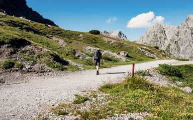 A man with a backpack walks along a mountain path. Walks along a rocky path against the sky and clouds. Traveling with a backpack.