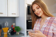 © fotofabrika - Pretty young woman in casual clothes using her smartphone in kitchen