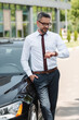 © LIGHTFIELD STUDIOS - Handsome businessman looking at wristwatch near car on urban street