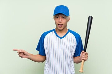 Wall Mural - Young asian man playing baseball over isolated green background surprised and pointing finger to the side