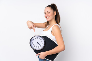 Wall Mural - Young brunette woman over isolated white background holding a weighing machine and pointing it