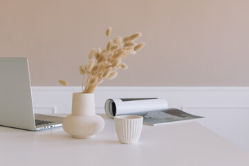 Laptop, vase with flowers, magazine on the table. Modern workplace. Minimal style.