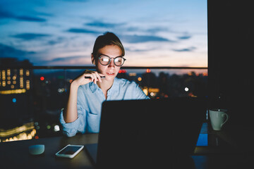 Wall Mural - pensive female freelancer working on publication for share on web page sitting with laptop at deskto