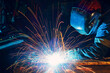 © primipil - Welder welding metal construction on factory. Long traces of sparks.