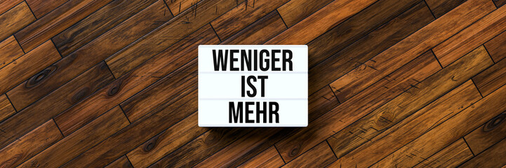 Wall Mural - lightbox with German message for LESS IS MORE on wooden background